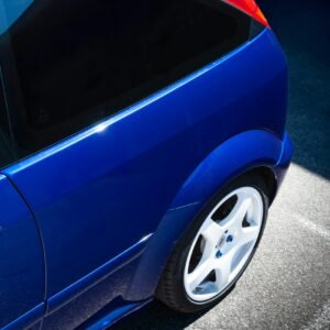 Close-up of a blue sports car with white rims shining in sunlight, outdoors.